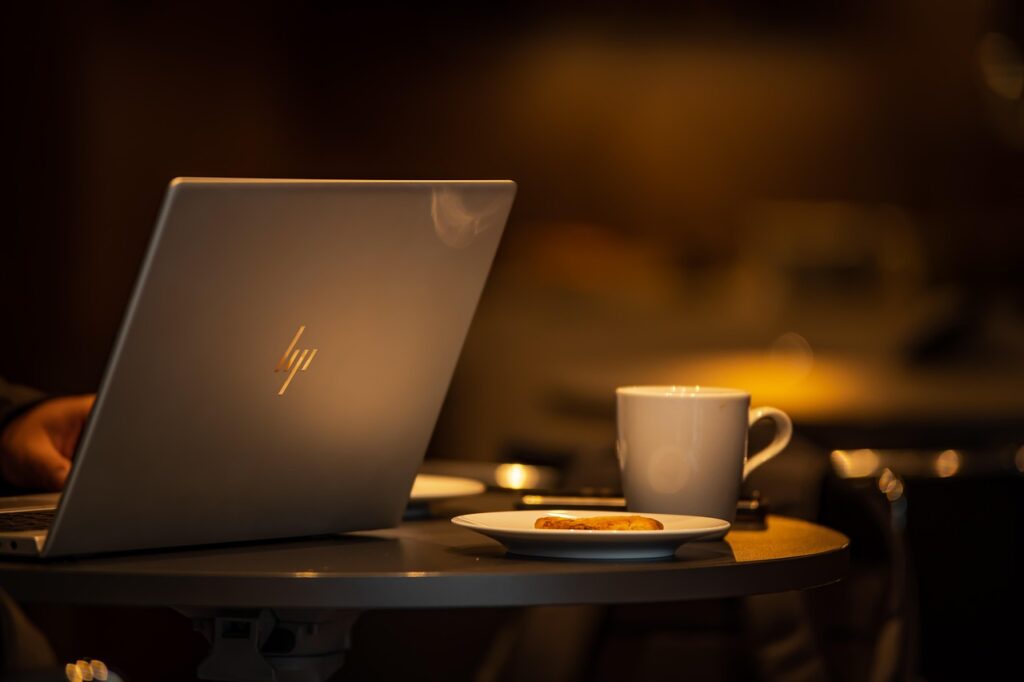 A warmly lit workspace with a laptop, coffee cup, and small plate, symbolizing comfort, curiosity, and structure in everyday work.