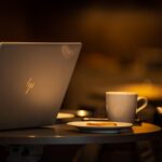 A warmly lit workspace with a laptop, coffee cup, and small plate, symbolizing comfort, curiosity, and structure in everyday work.
