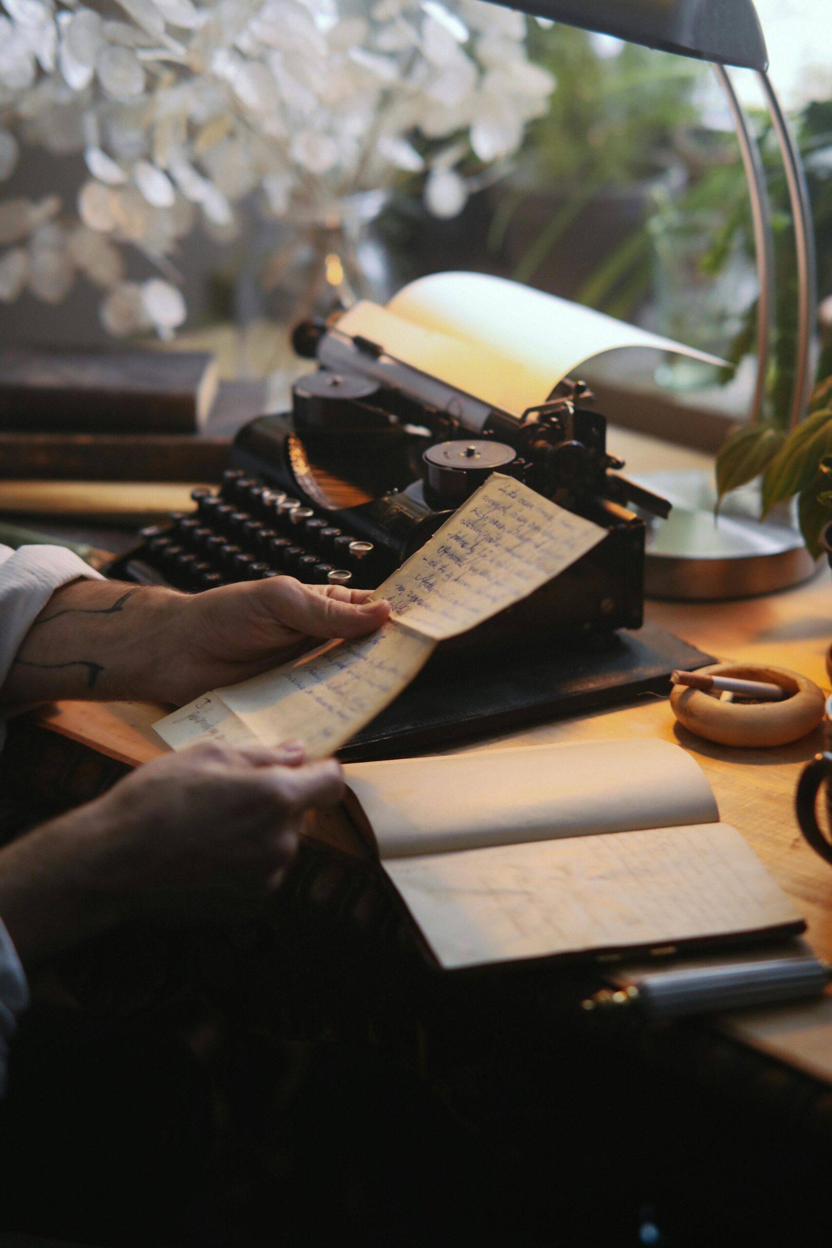 A person holding a handwritten paper beside a typewriter on a desk