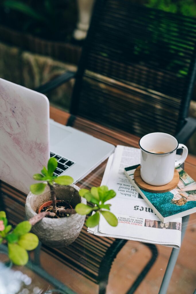 A digital gardener’s workspace with a laptop, coffee mug, and potted plant on a glass table in the garden, symbolizing balance between technology and nature.