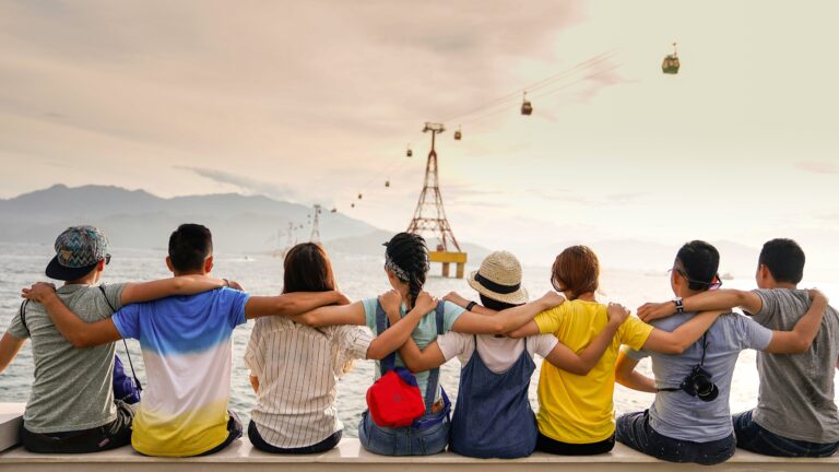 A group of travelers sitting arm in arm at the edge of the water, symbolizing connection and group travel planning.