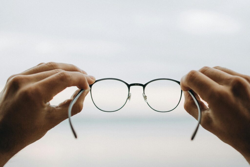 A person holding black-framed eyeglasses, symbolizing clarity and perspective for AI in context