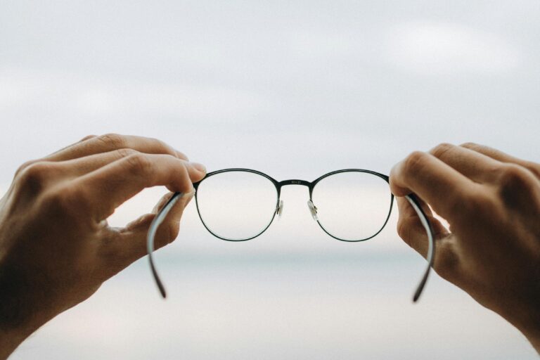A person holding black-framed eyeglasses, symbolizing clarity and perspective for AI in context