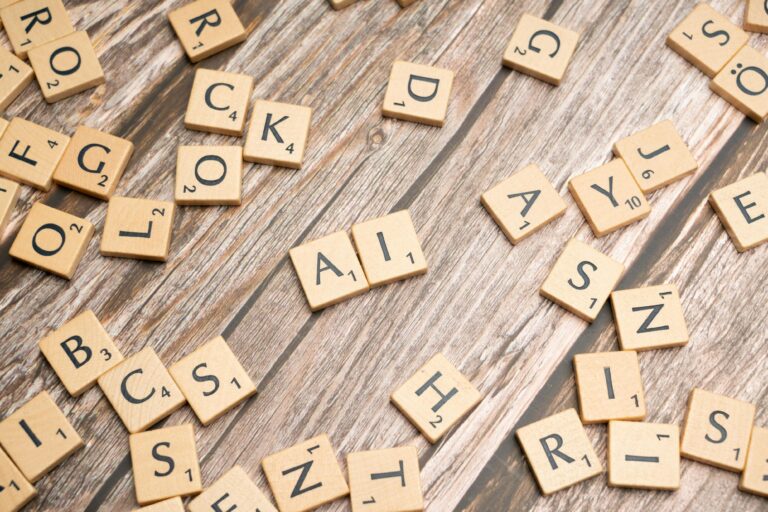 Scrabble tiles scattered across a wooden table with the letters A and I placed together in the center, representing AI prompt fluency and the art of structured language.