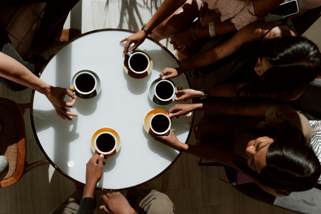 A group of people seated around a circular table, each holding a cup of coffee, symbolizing connection and shared understanding